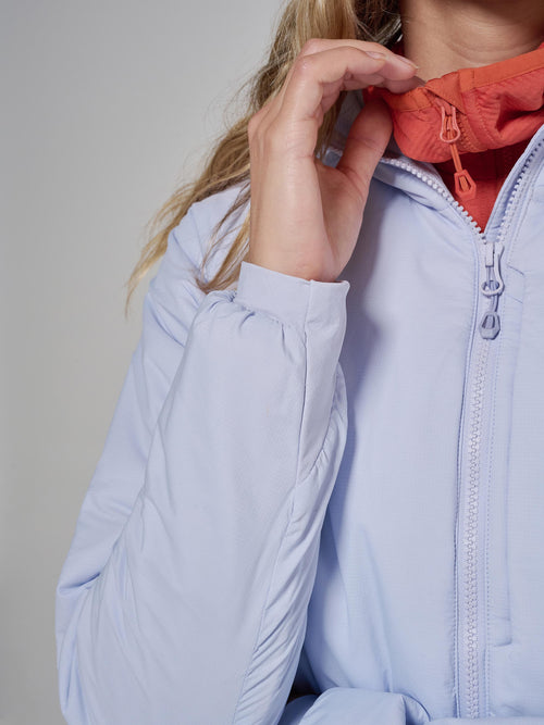 Close-up of a person wearing a light periwinkle blue puffer jacket, pulling up an orange hood over the collar.