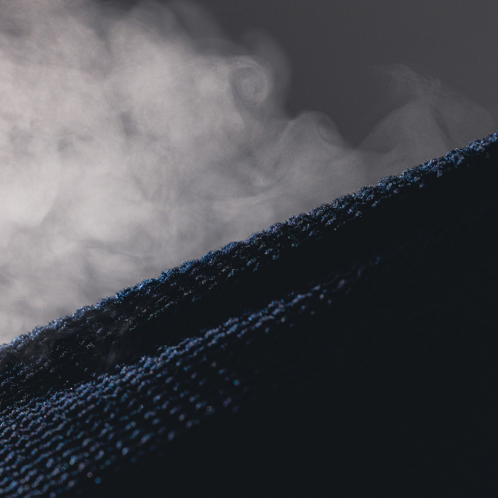 Close-up of a dark navy textured fabric with visible steam or vapor rising through it against a dark gray background.