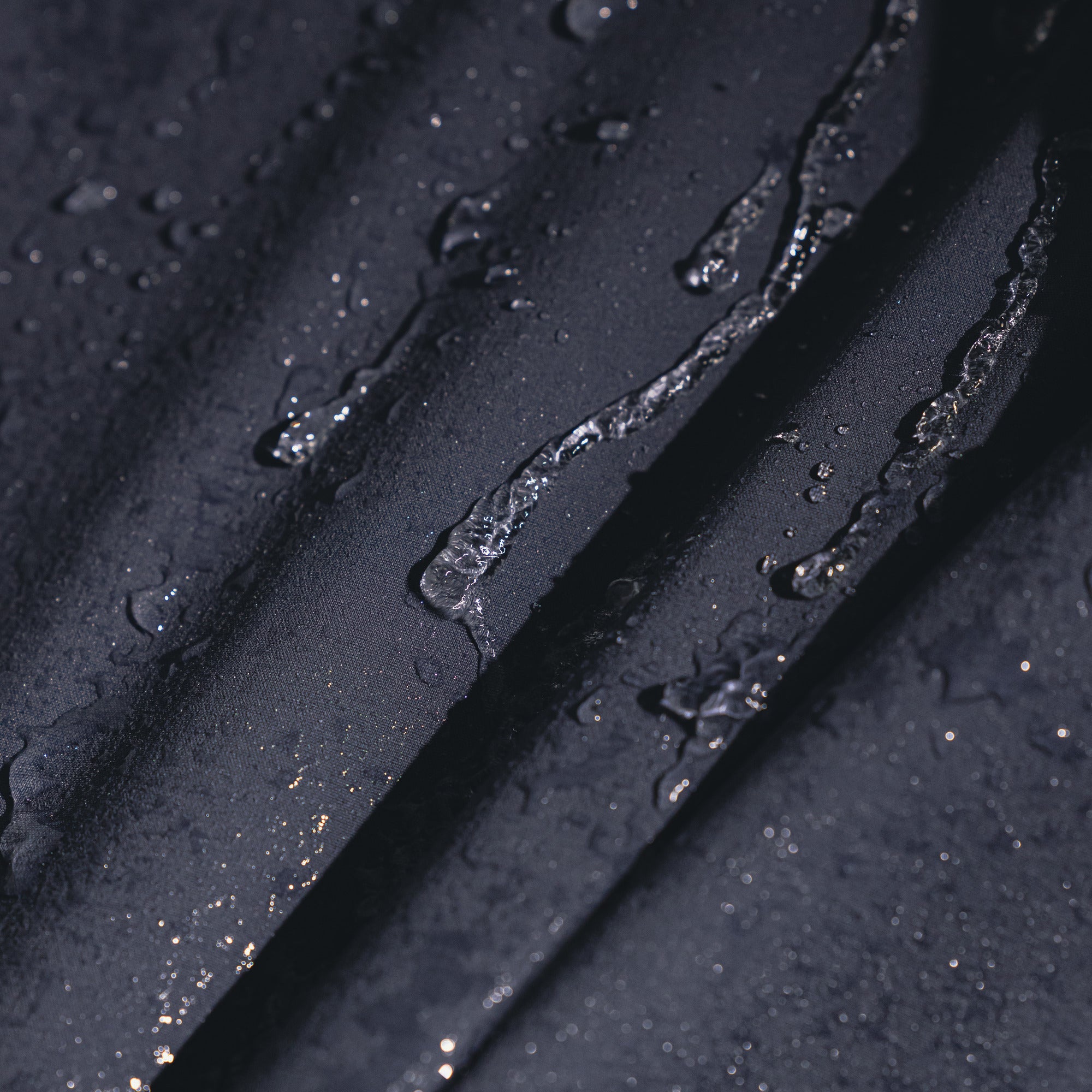 Close-up of a dark, water-repellent textured surface with water droplets and streaks running across it.