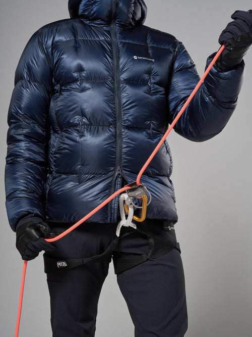 Person wearing a dark blue puffer jacket holding climbing equipment on a gray background